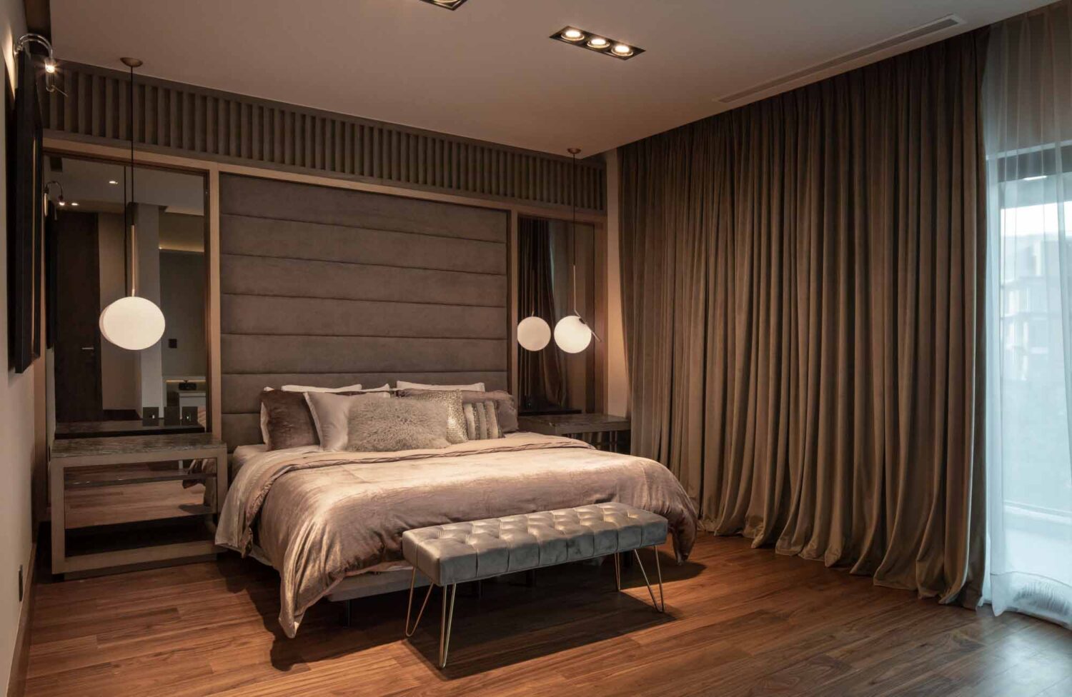 Esta imagen muestra un dormitorio elegante y acogedor. El dormitorio está decorado con lujo y cuenta con una cama grande, dos mesitas de noche y cortinas. La cama está hecha y tiene almohadas sobre ella. Las mesitas de noche tienen lámparas y otros objetos decorativos. Las cortinas son de color claro y bloquean la luz.